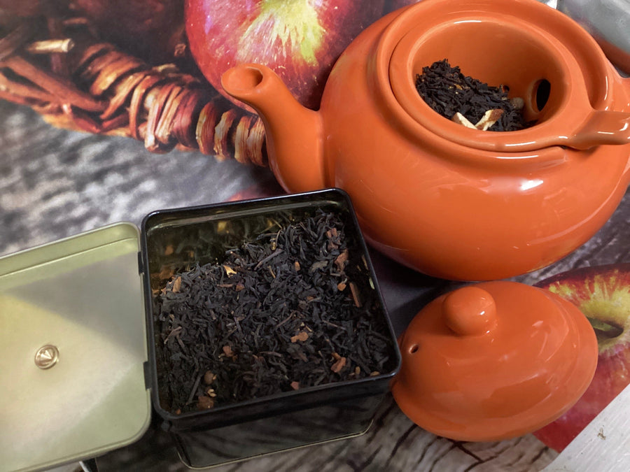 orange teapot with a black container of black tea. Apples in a basket in the background