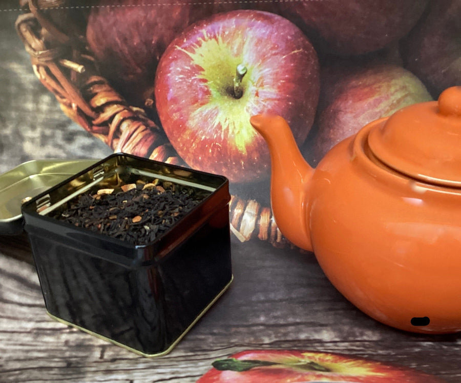 orange teapot with black tea in a black container with apples in a basket background 